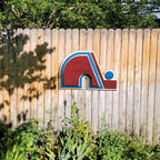Wooden Nordique logo in 3D, painted in red, blue, and white on a wooden fence surrounded by greenery