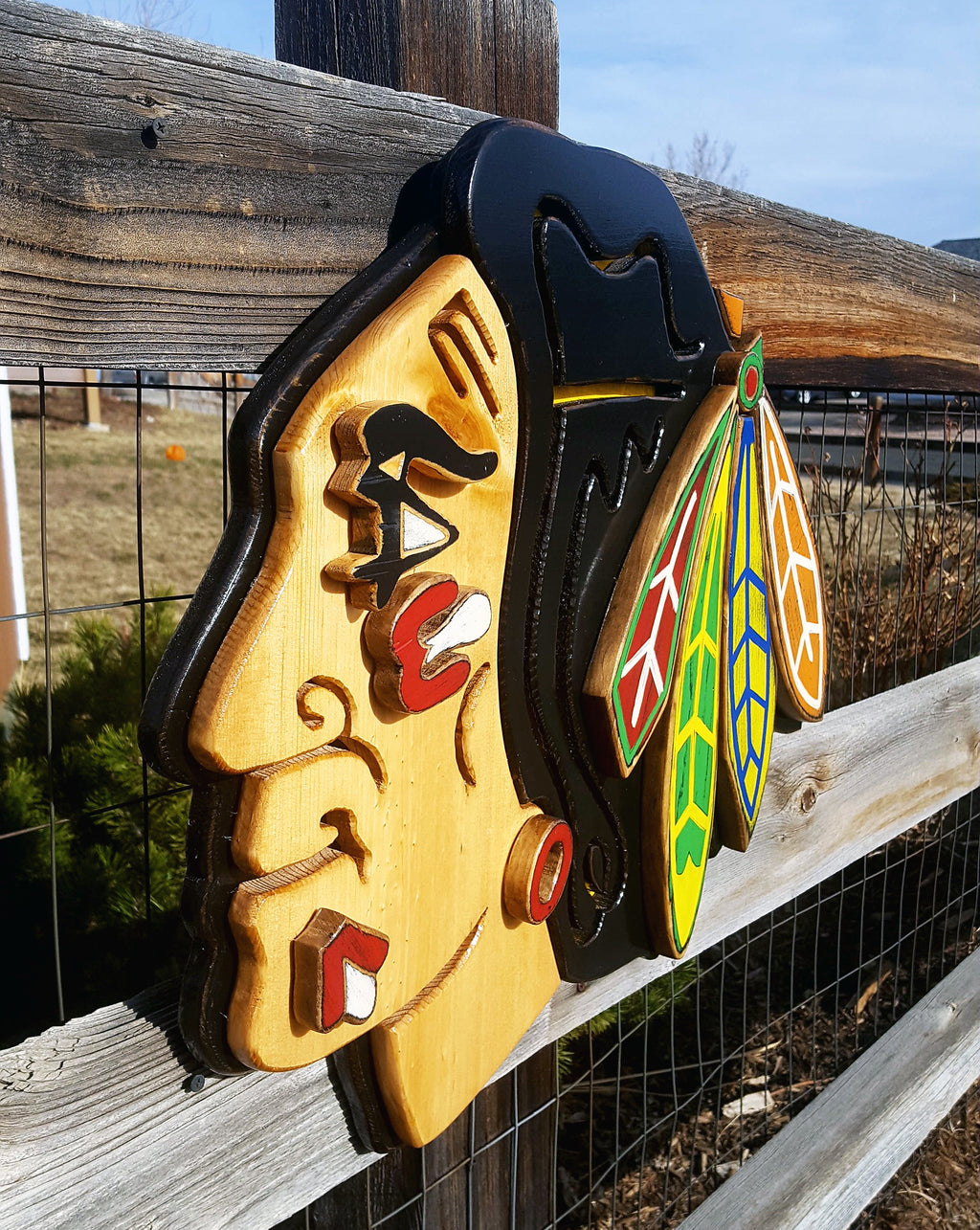 Decorative wooden Native American with colorful feather design on a wooden fence