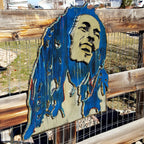 Wooden sculpture of Bob Marley's face and hair in blue and brown tones on a wooden background