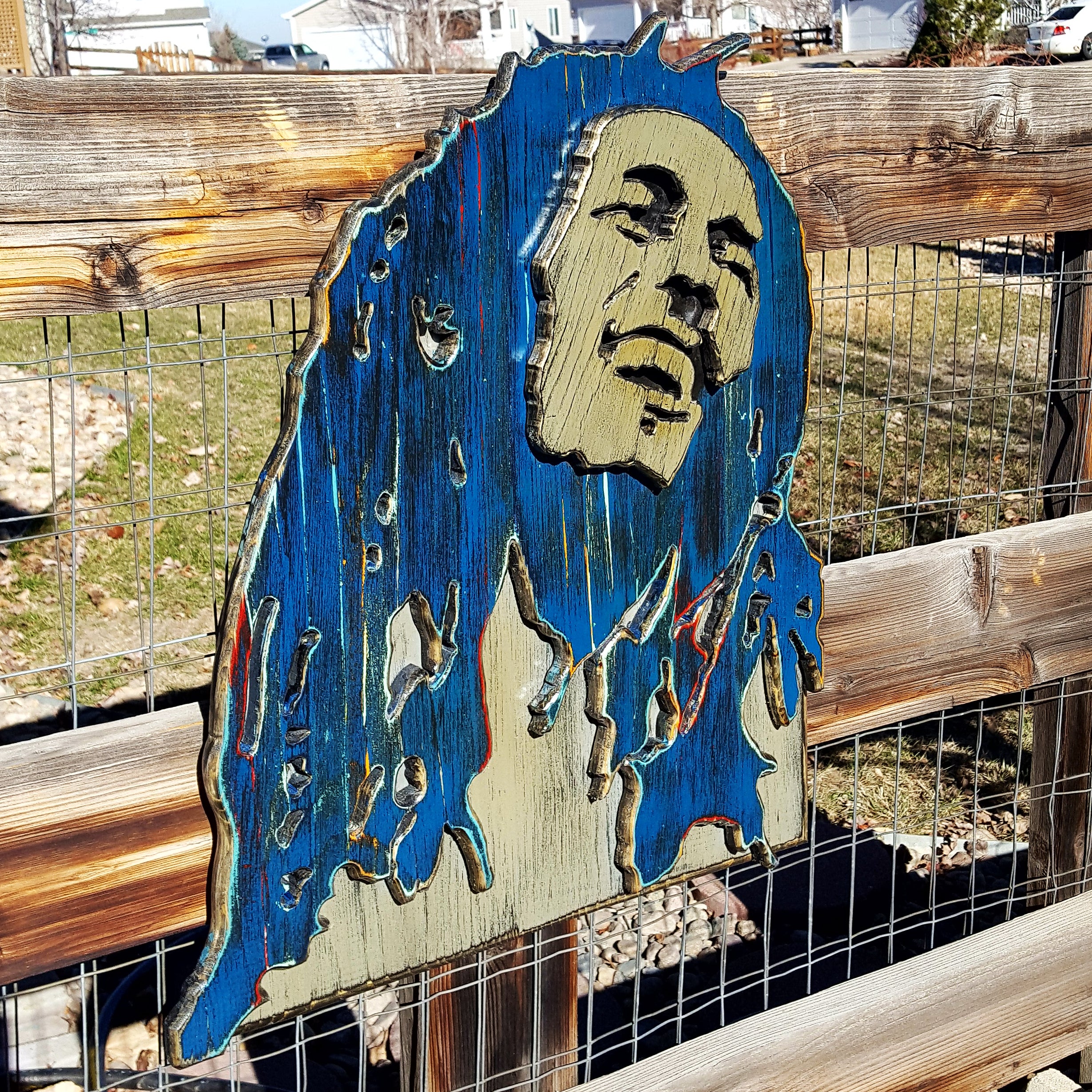 Wooden sculpture of Bob Marley's face and hair in blue and brown tones on a wooden background