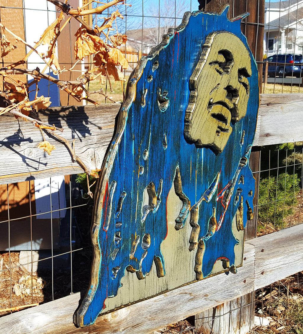 Wooden sculpture of Bob Marley's face and hair in blue and brown tones on a wooden background