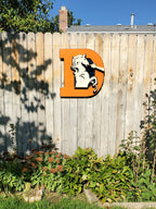 Wooden Broncos Retro "D" logo displayed on a wooden fence surrounded by trees and greenery 