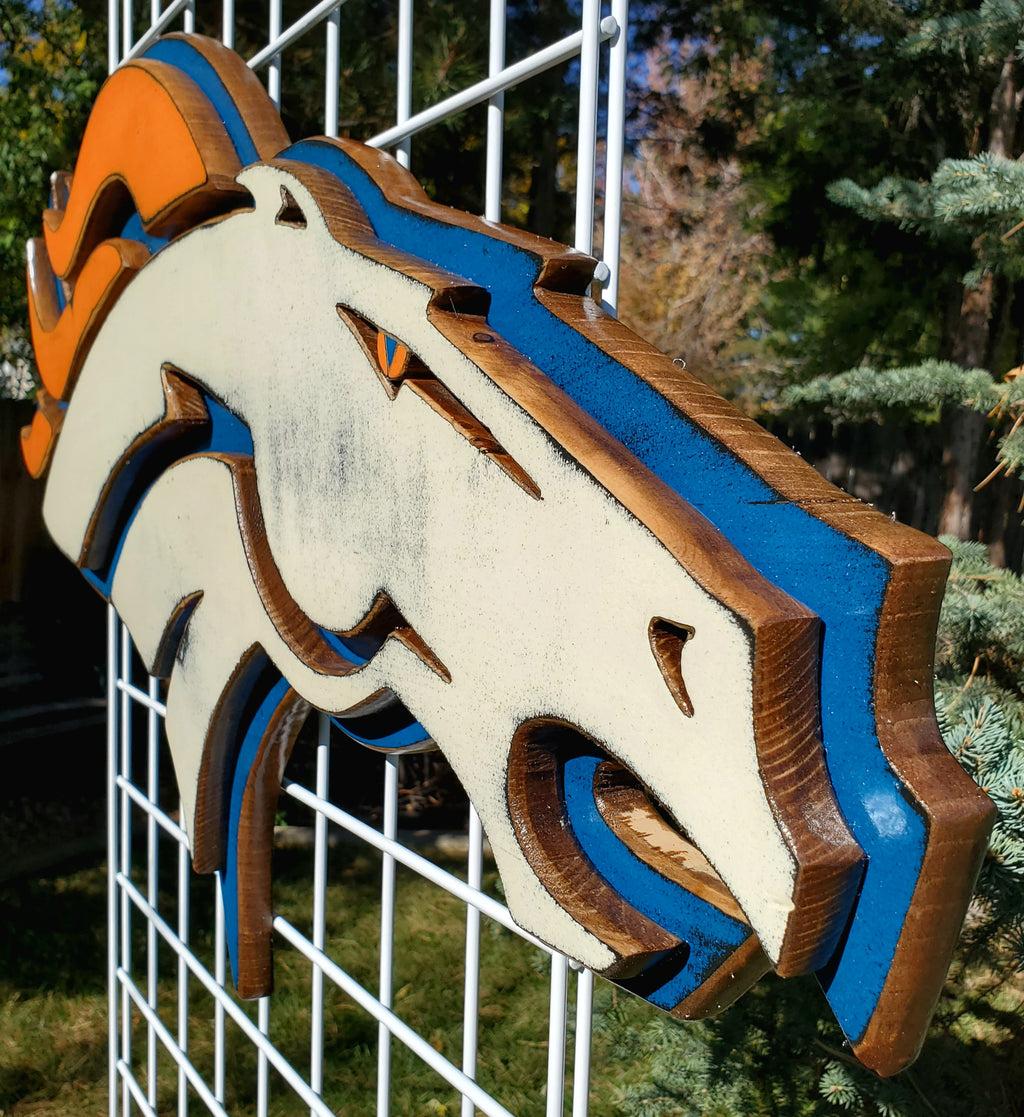 Denver Broncos modern logo displayed on a metal grid with trees in the background
