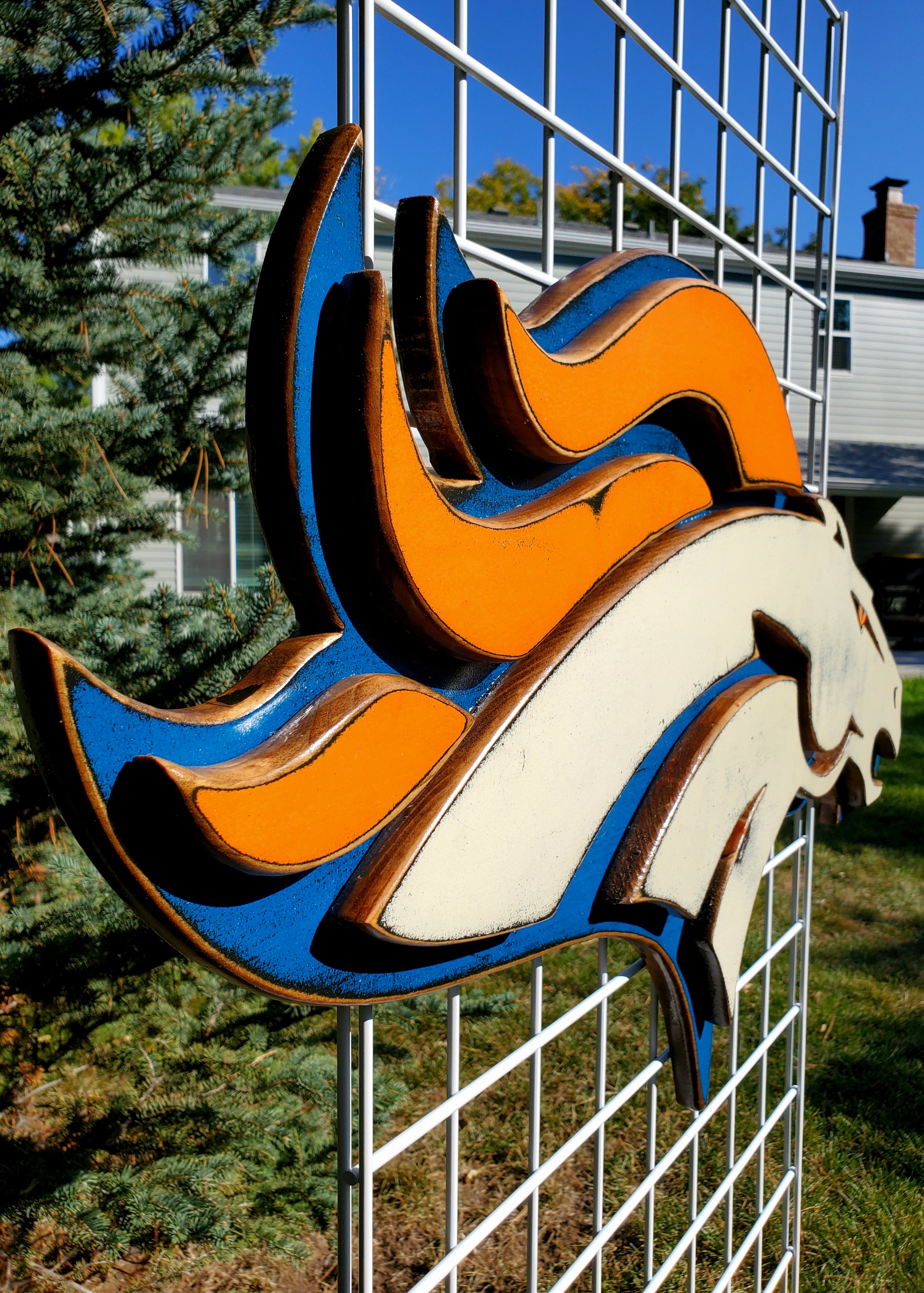 Denver Broncos modern logo on a metal grid with trees and house in the background