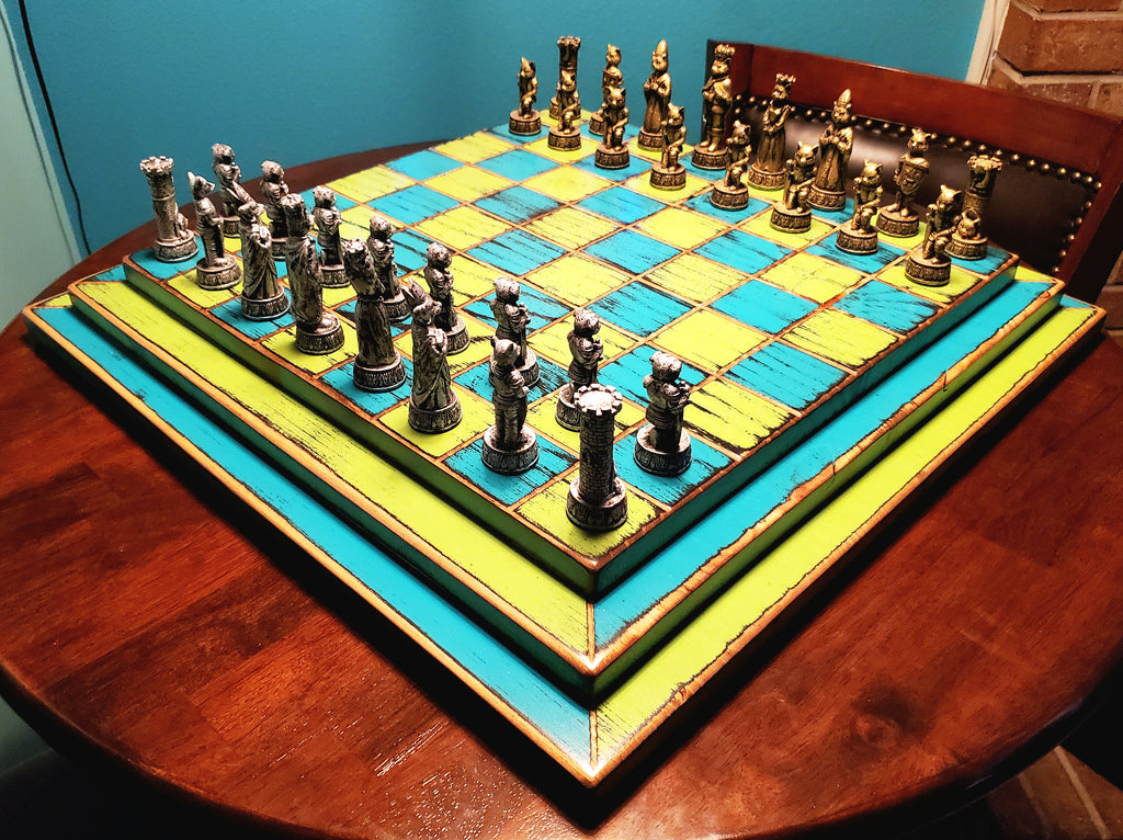 Colorful blue and yellow chessboard with pieces on a round wooden table set against a blue wall.