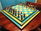 Colorful blue and yellow chessboard with pieces on a round wooden table set against a blue wall.