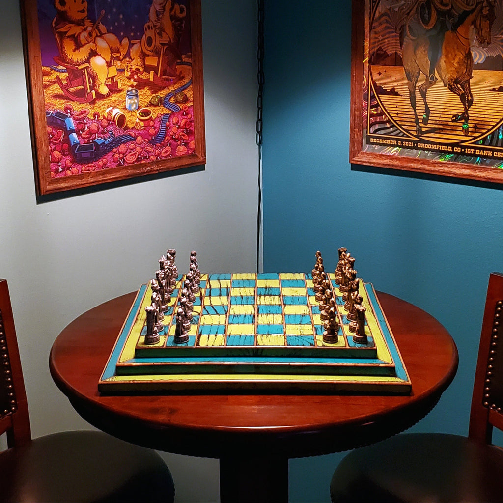 Chessboard on a round wooden table with framed posters hanging on the wall in the background