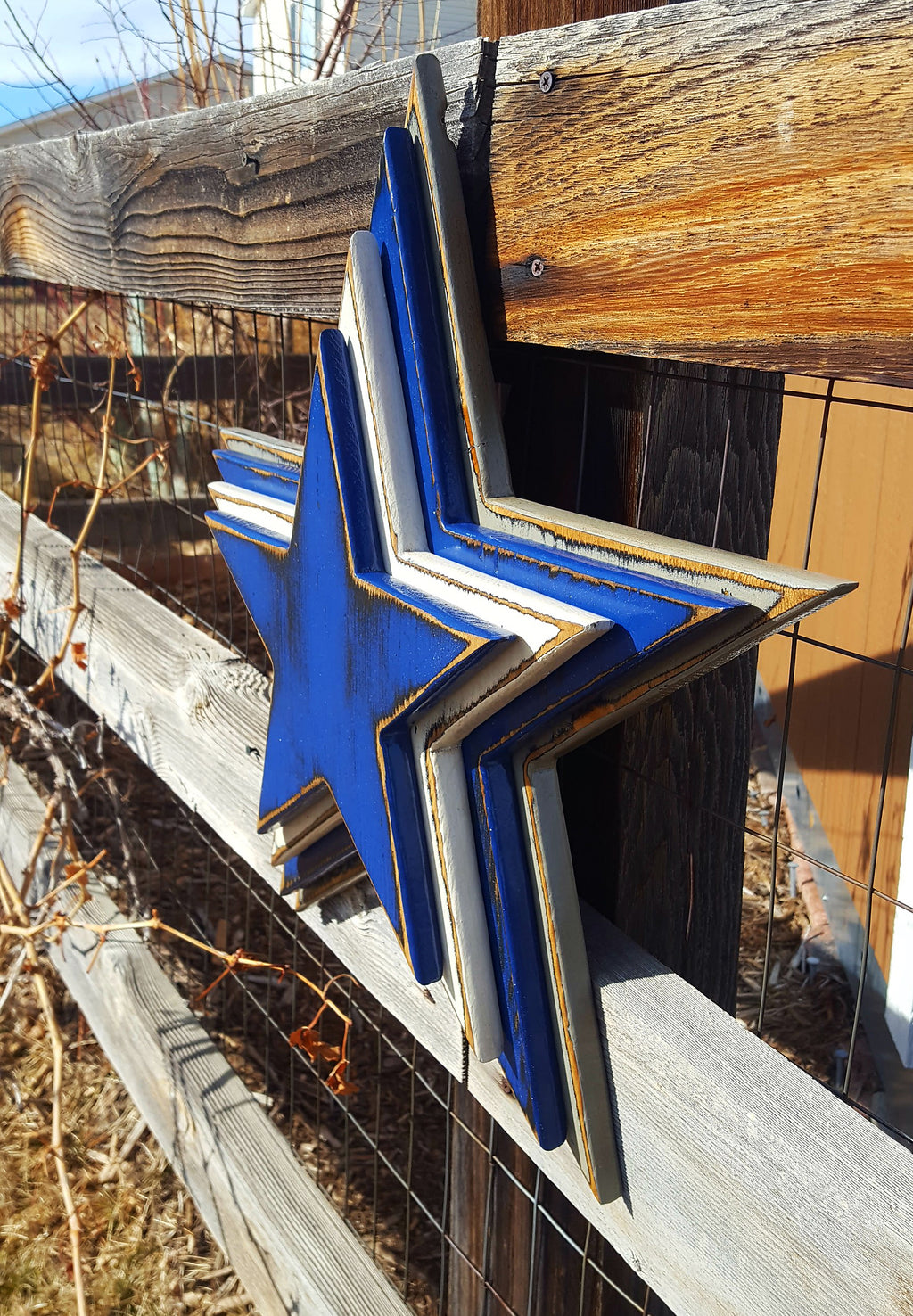 Cowboys star logo with four wooden layers alternating blue, white, blue, gray and displayed on a wooden fence.