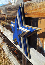 Cowboys star logo with four wooden layers alternating blue, white, blue, gray and displayed on a wooden fence.