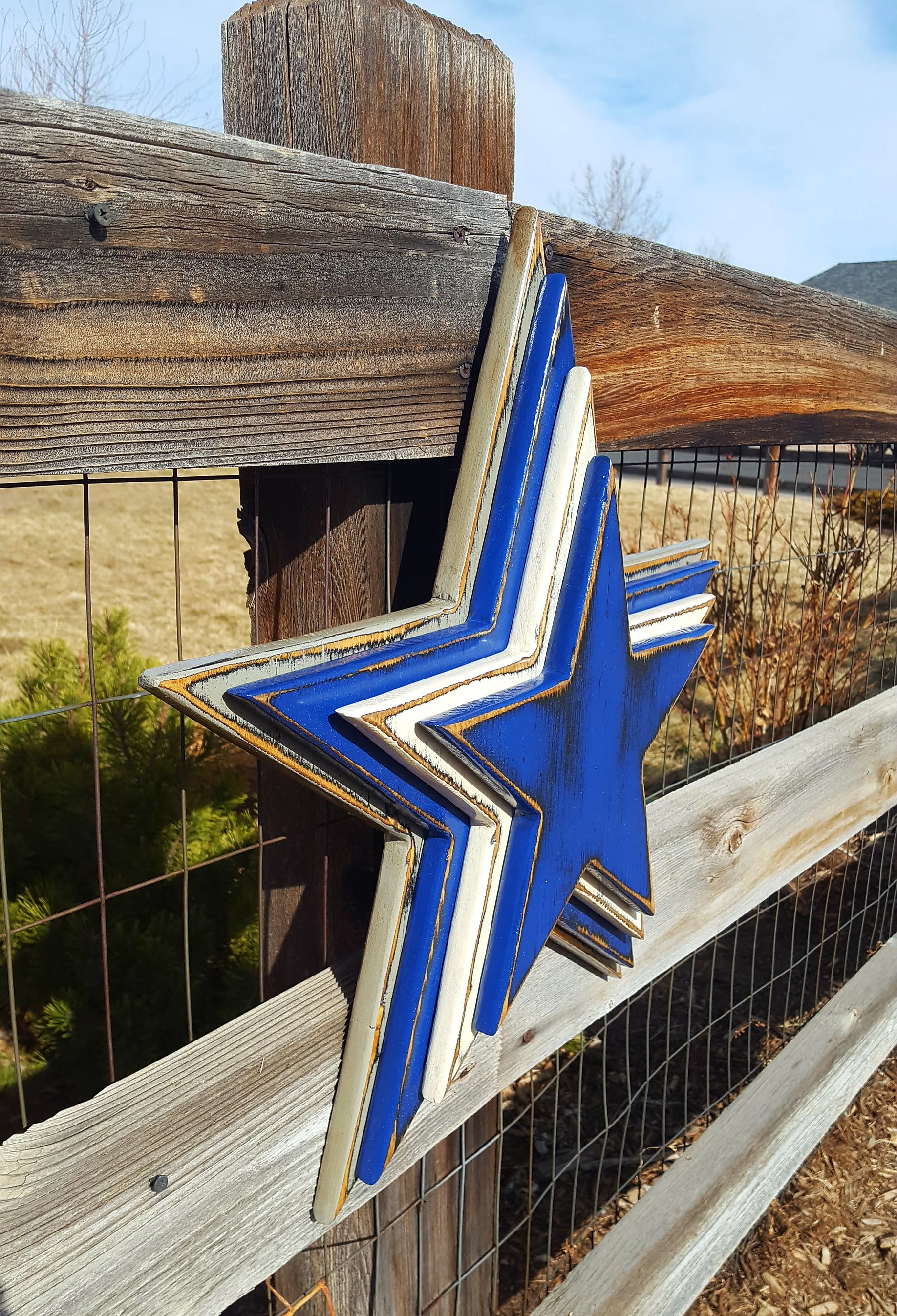 Cowboys star logo with four wooden layers alternating blue, white, blue, gray and displayed on a wooden fence.