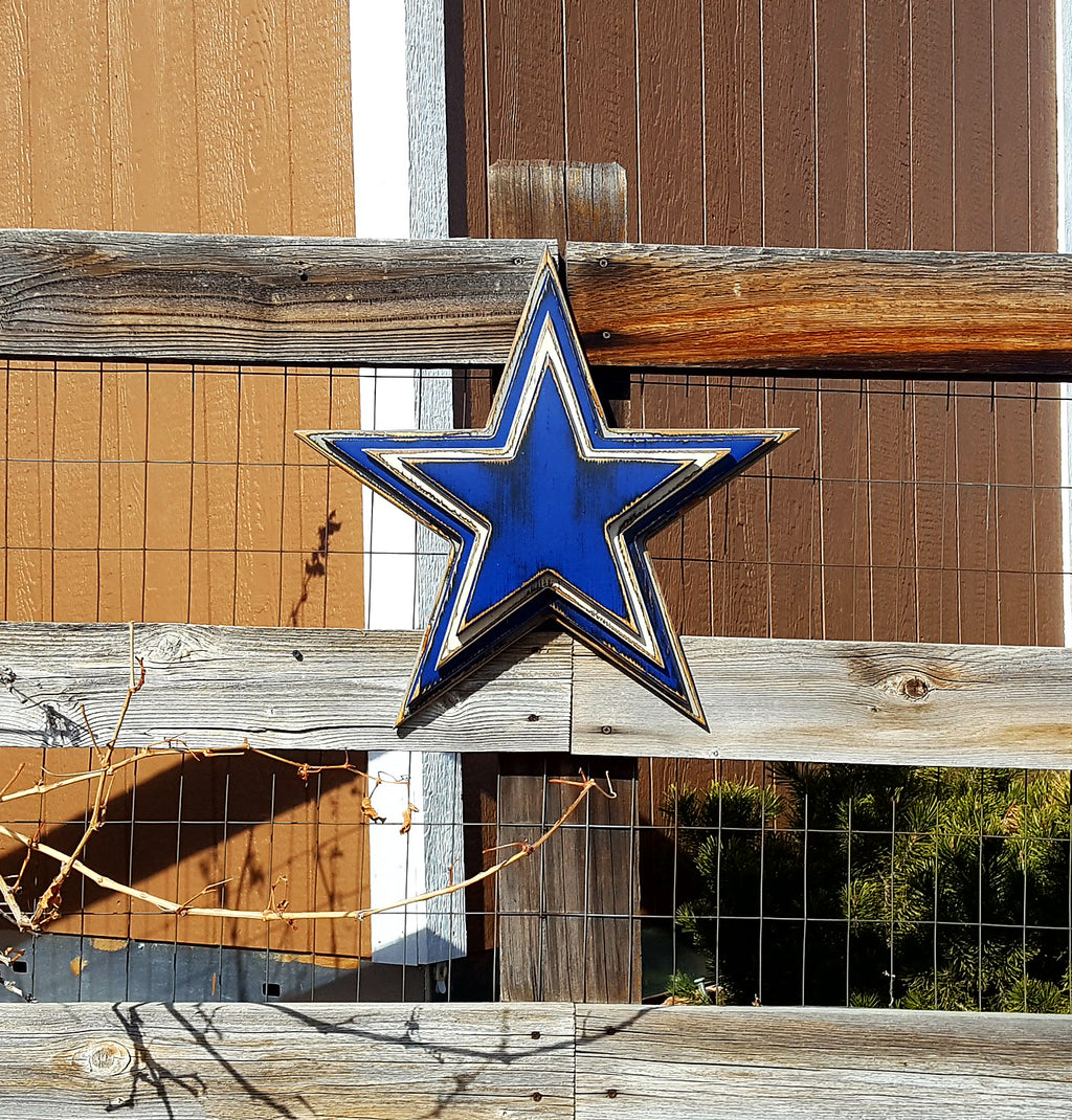 Cowboys star logo with four wooden layers alternating blue, white, blue, gray and displayed on a wooden fence.
