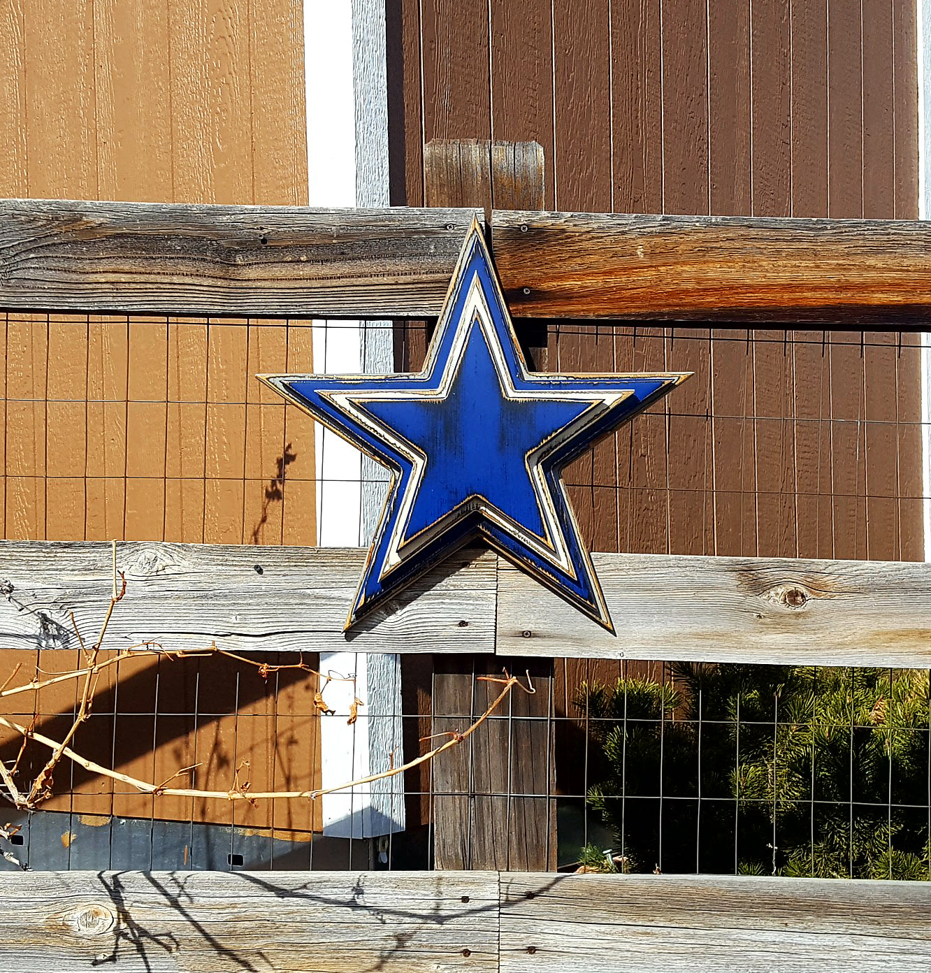 Cowboys star logo with four wooden layers alternating blue, white, blue, gray and displayed on a wooden fence.