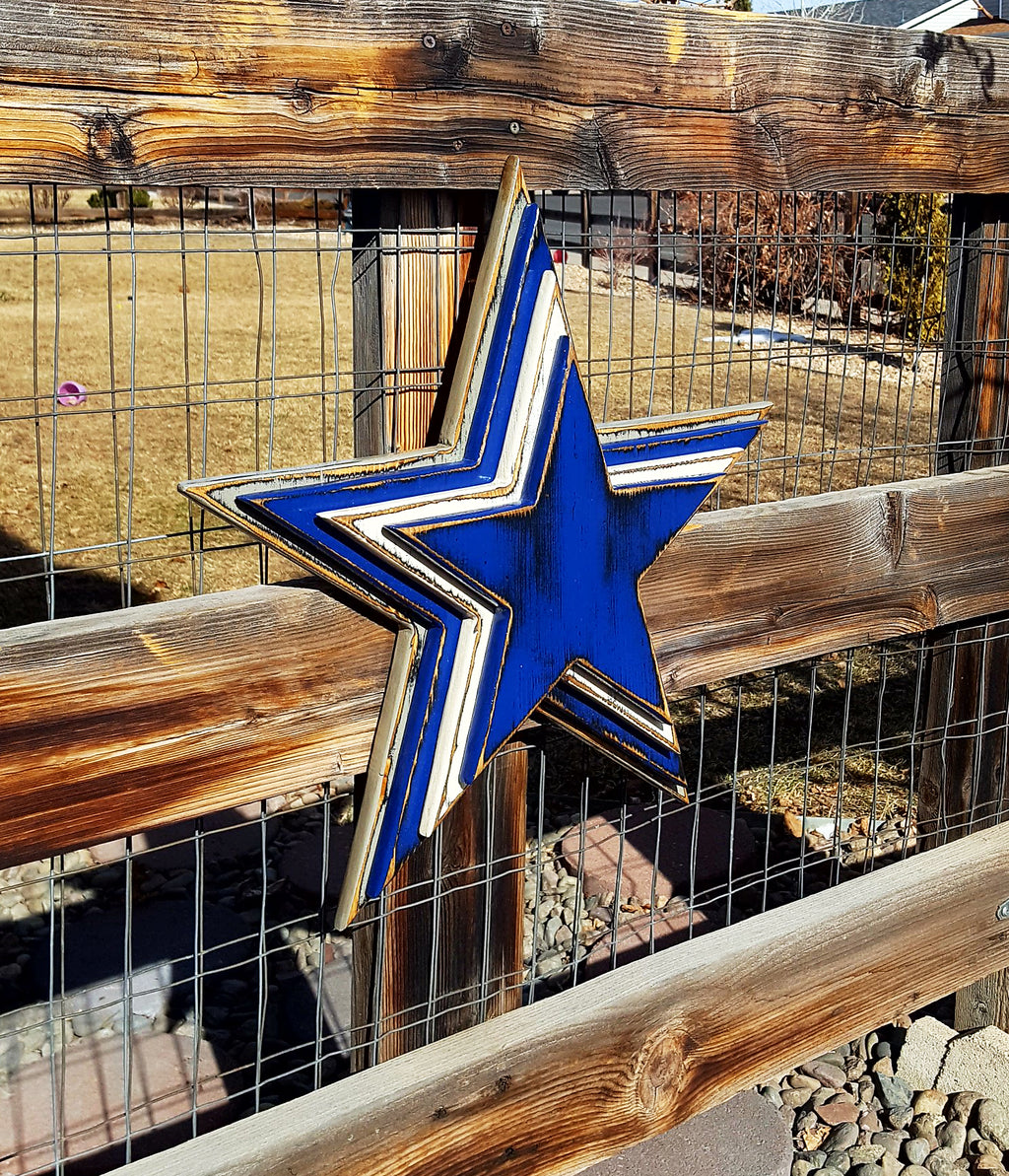 Cowboys star logo with four wooden layers alternating blue, white, blue, gray and displayed on a wooden fence.