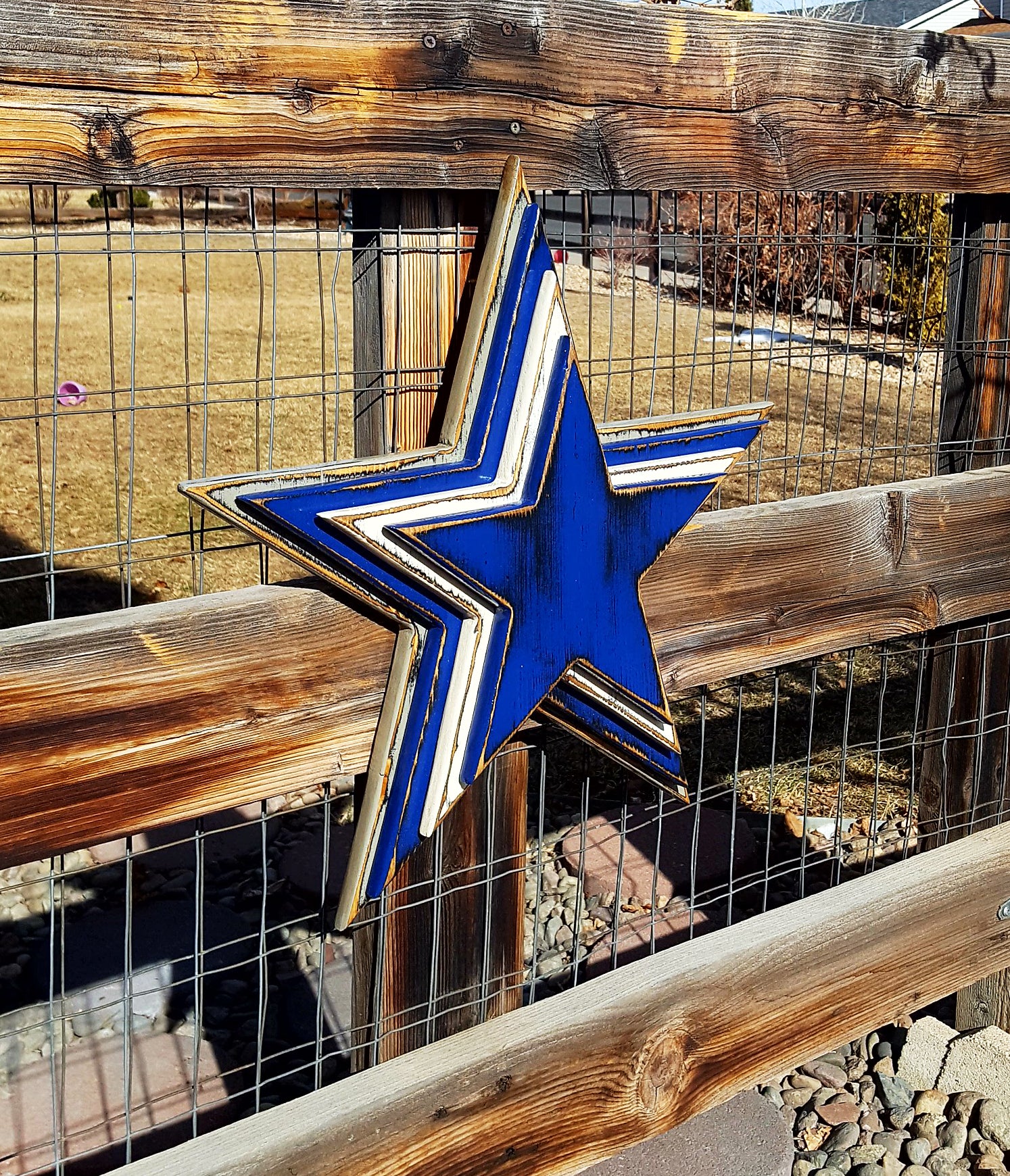 Cowboys star logo with four wooden layers alternating blue, white, blue, gray and displayed on a wooden fence.