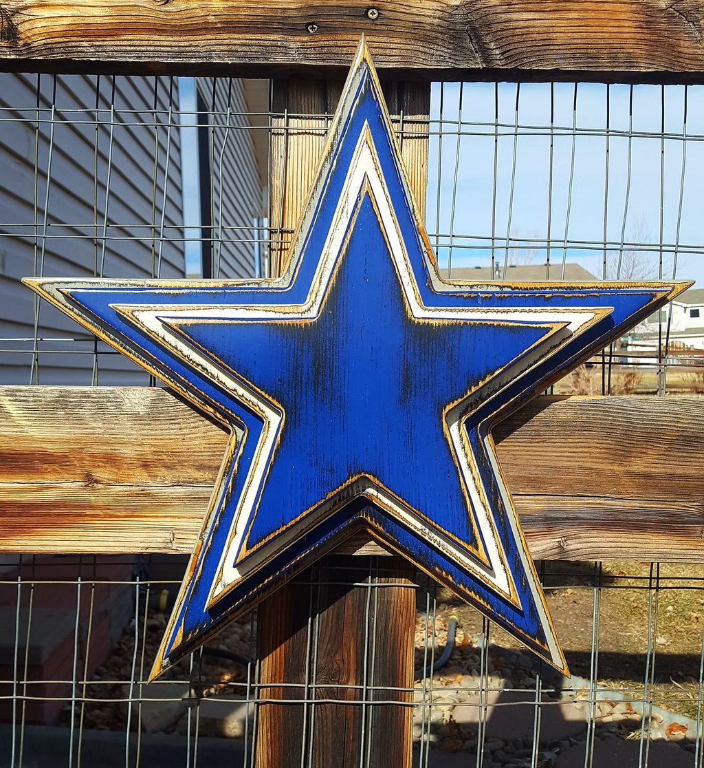Cowboys star logo with four wooden layers alternating blue, white, blue, gray and displayed on a wooden fence.