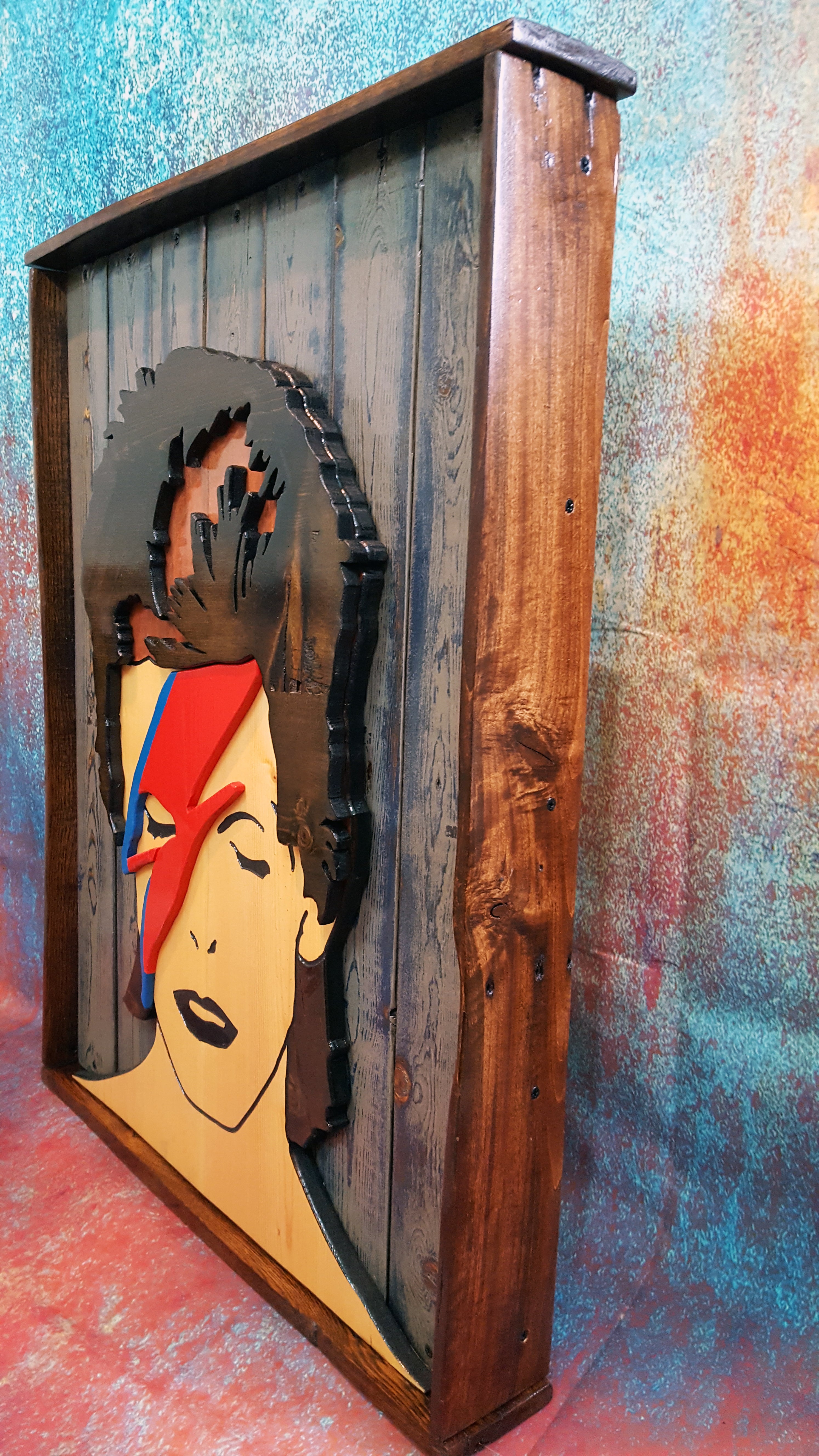 Wooden wall art of David Bowie's Aladdin Sane album cover photographed on a colorful backdrop