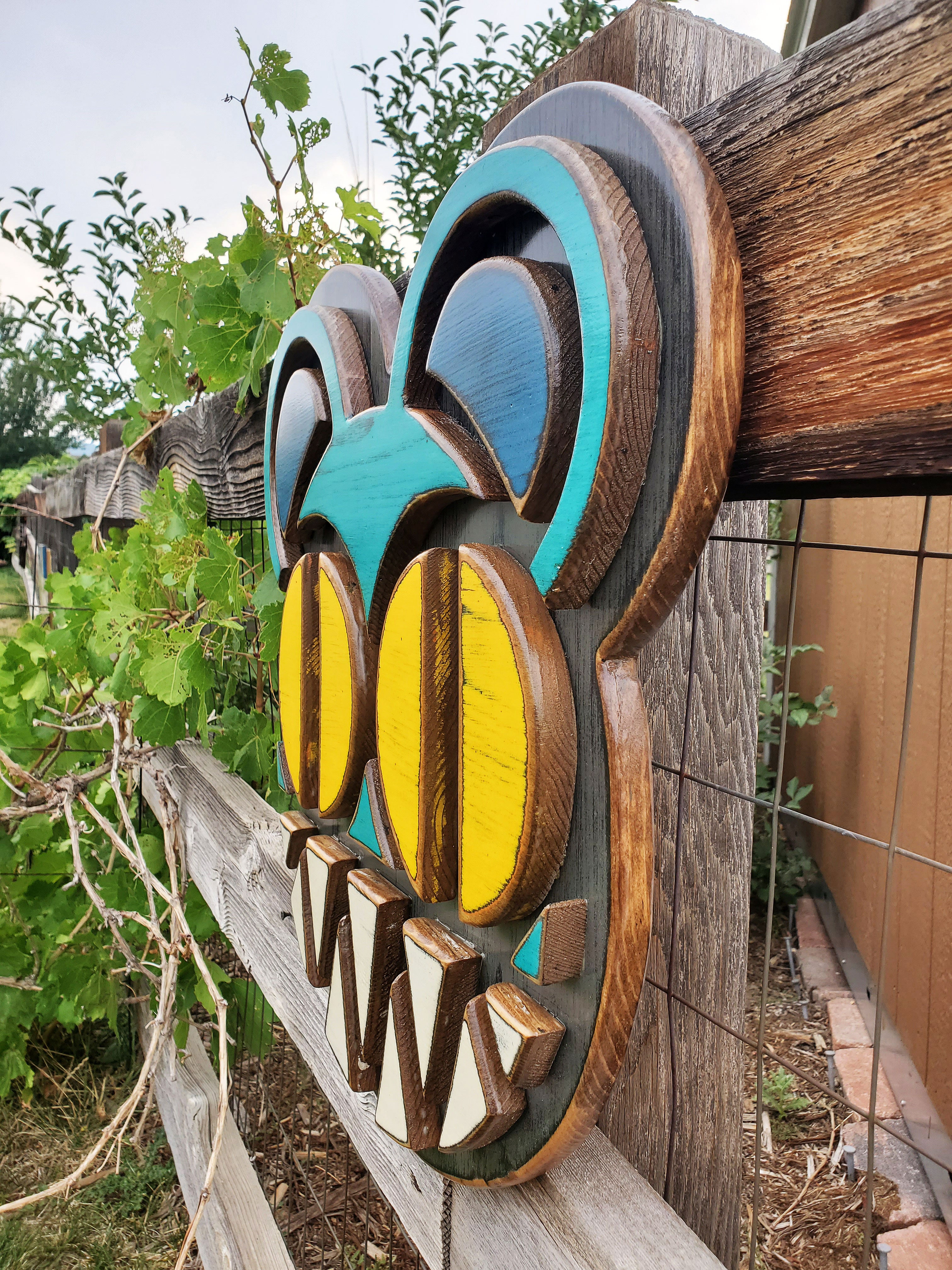 Decorative wooden wall art featuring Radiohead's Modified Bear logo on a wooden fence outdoors.
