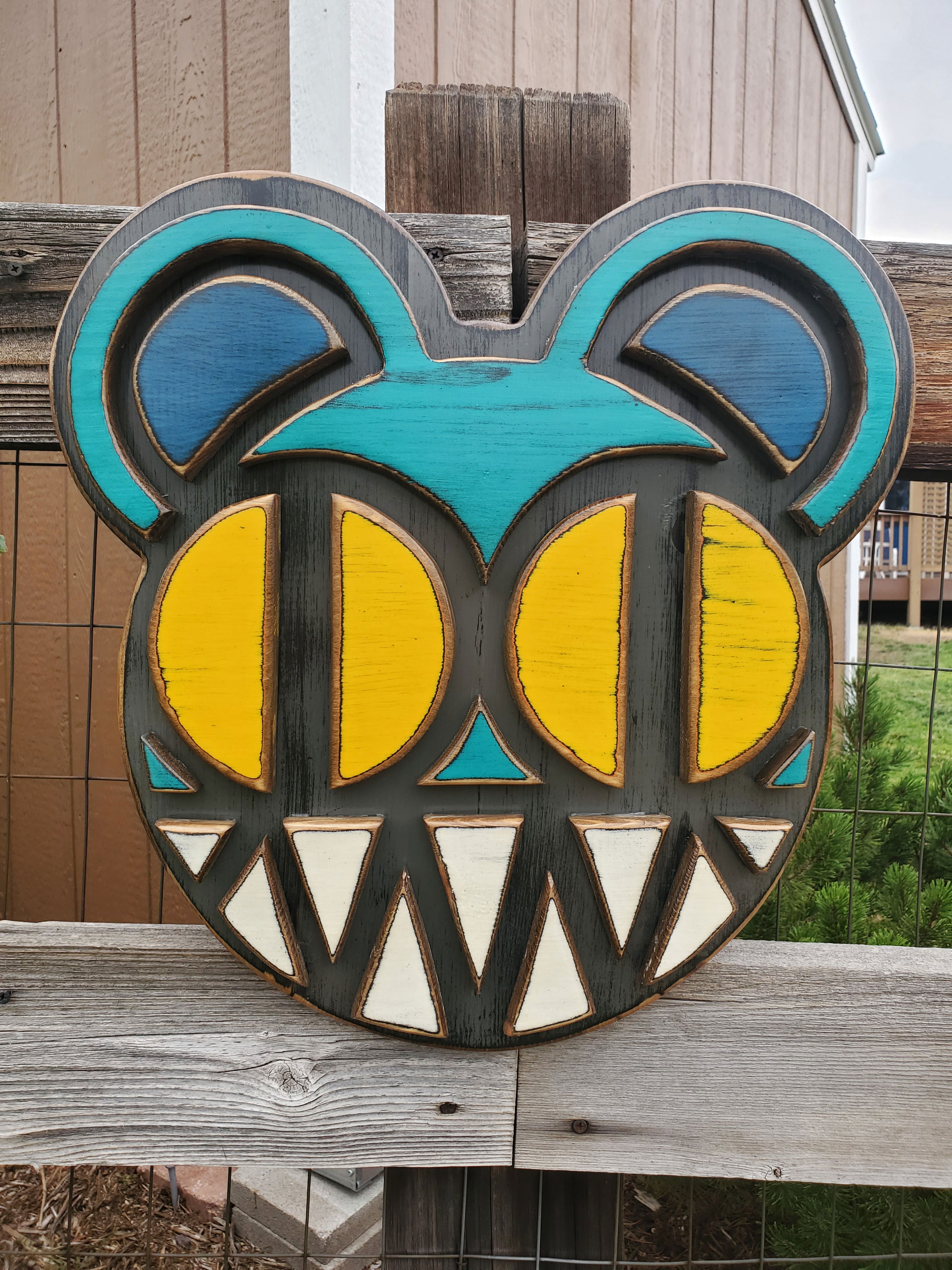 Decorative wooden wall art featuring Radiohead's Modified Bear logo on a wooden fence outdoors.