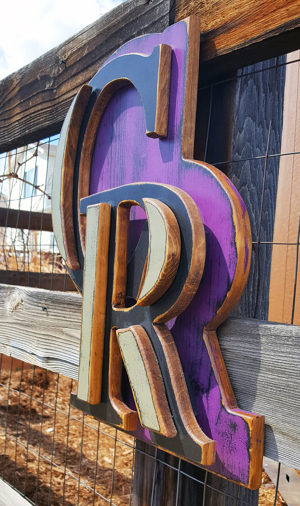 Decorative sign with Colorado Rockies "CR" logo with a purple background on a chicken wire fence