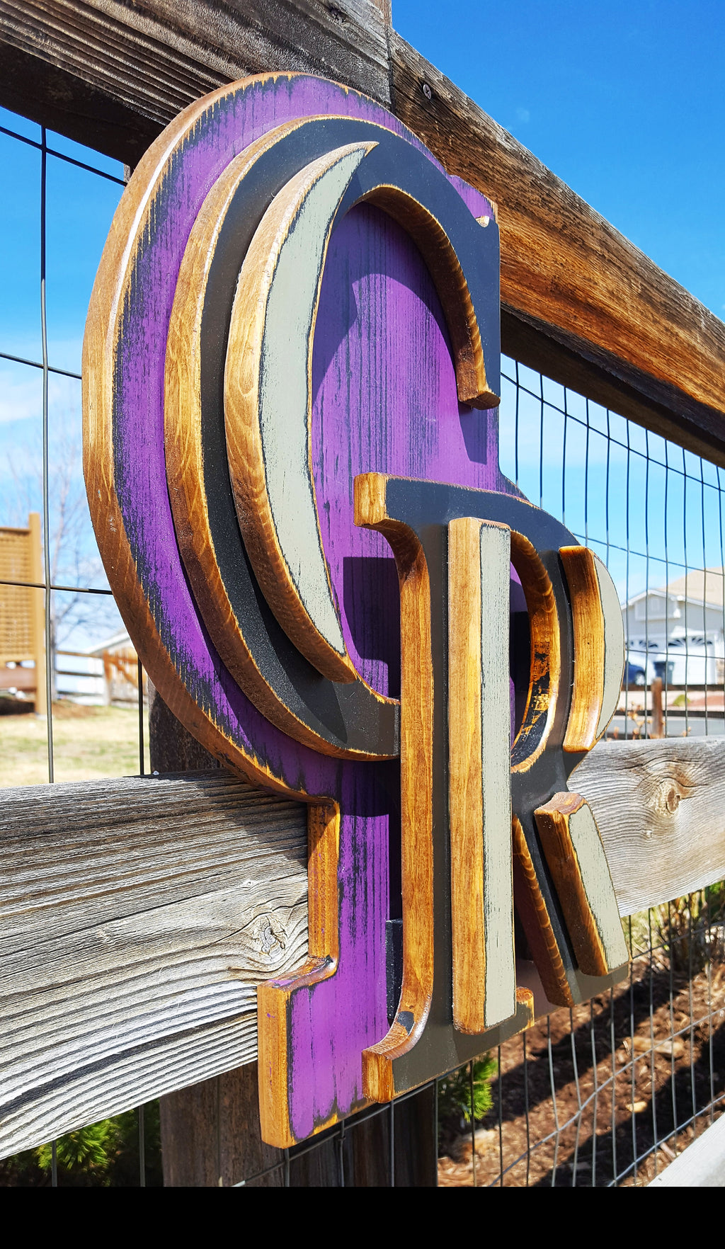 Decorative sign with Colorado Rockies "CR" logo with a purple background on a chicken wire fence