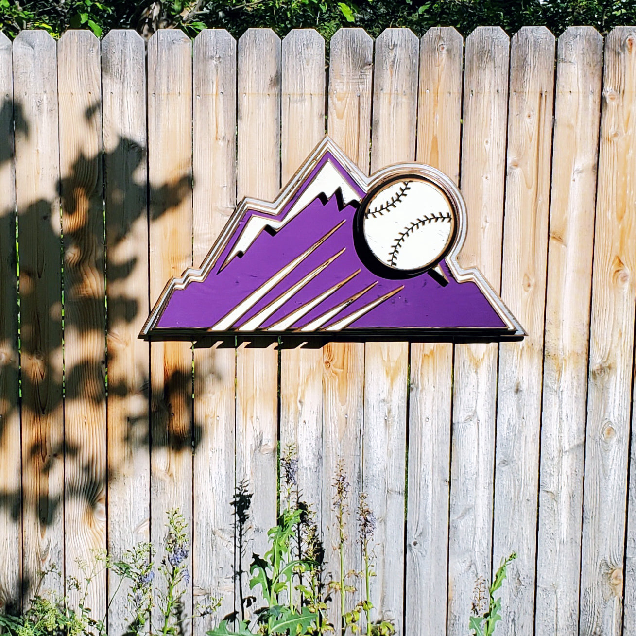 Decorative sign with Colorado Rockies purple mountain design and baseball on a wooden fence background