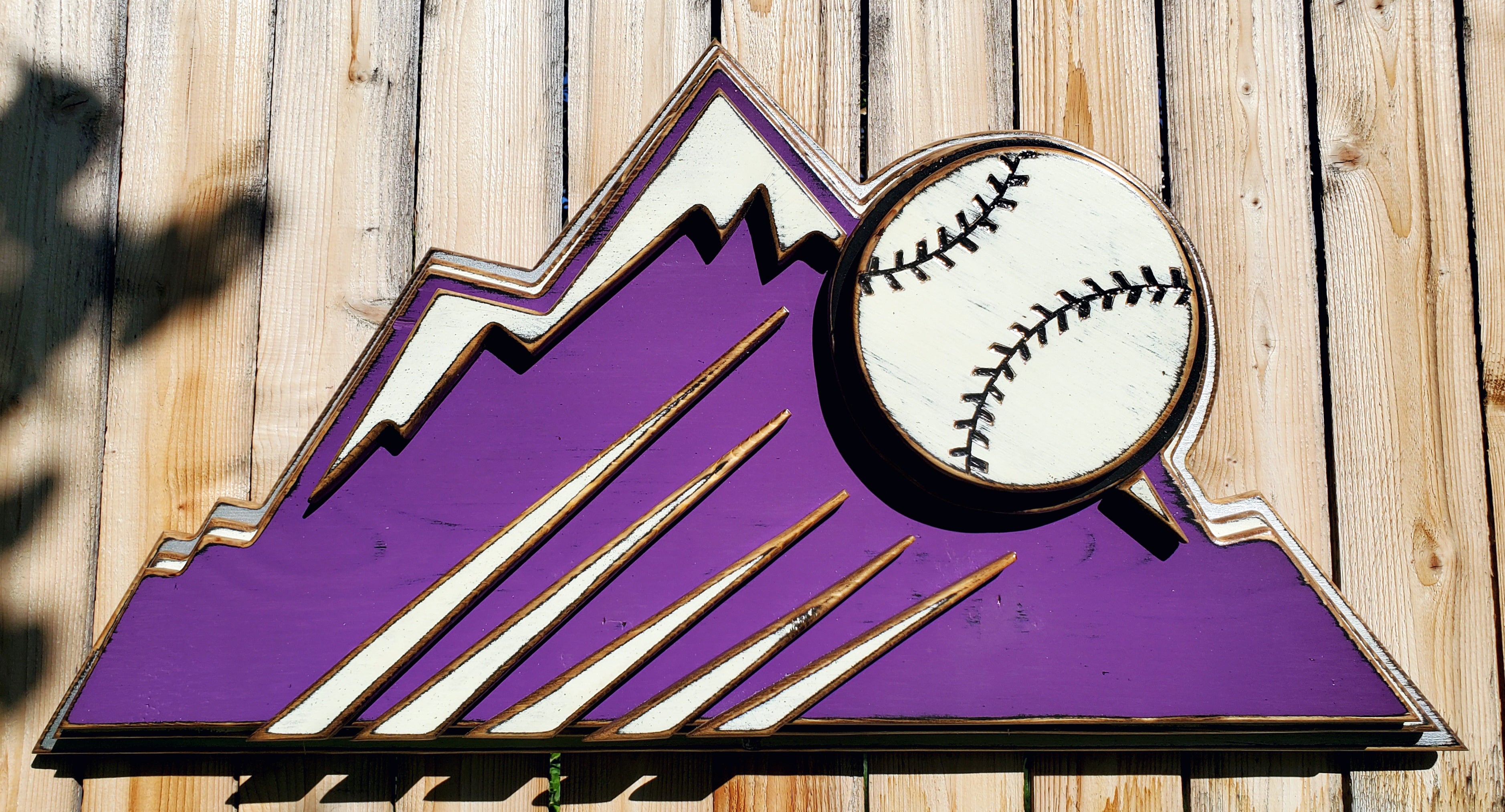 Decorative sign with Colorado Rockies purple mountain design and baseball on a wooden fence background
