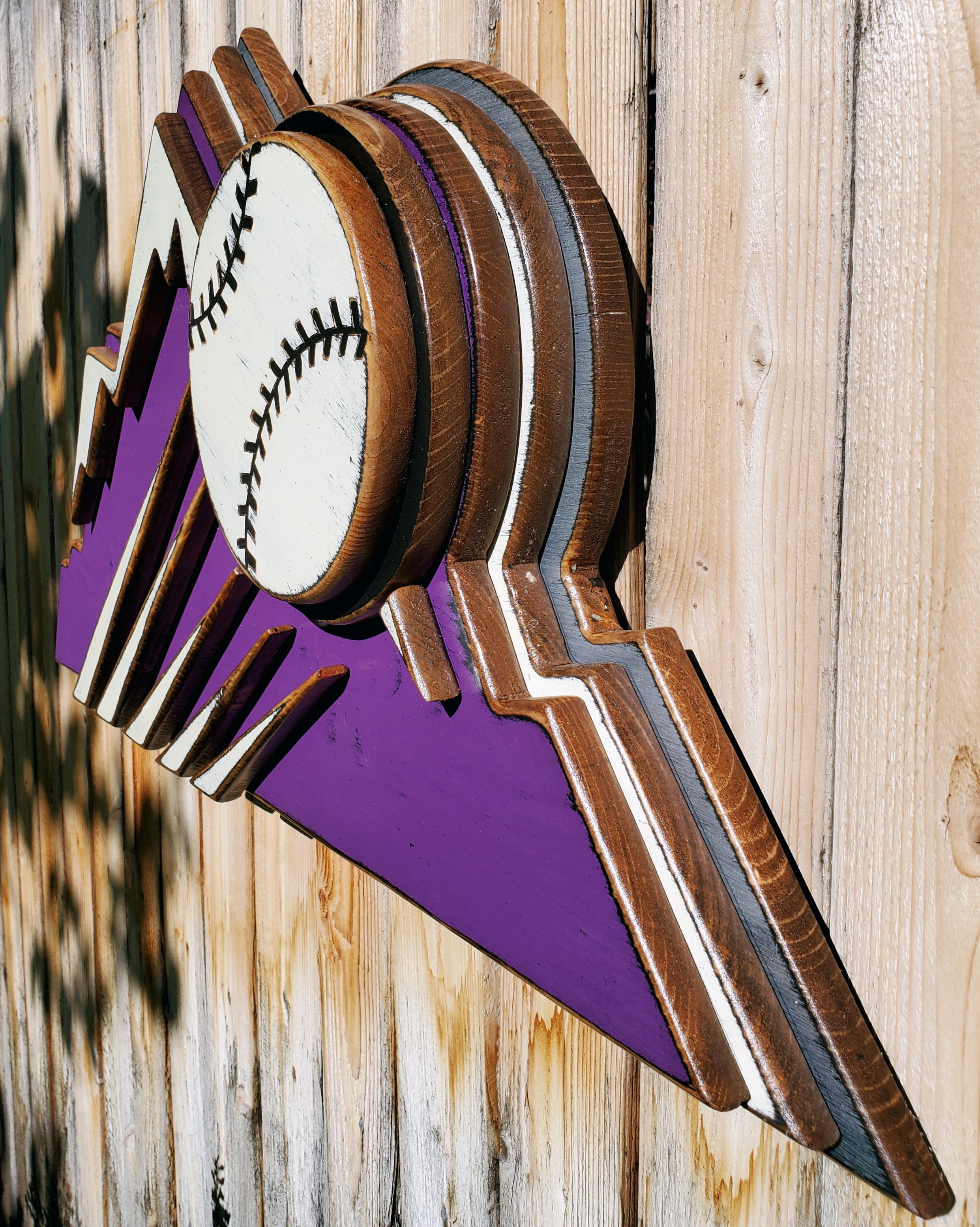 Decorative sign with Colorado Rockies purple mountain design and baseball on a wooden fence background