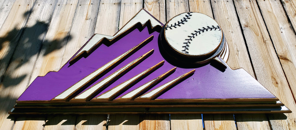 Decorative sign with Colorado Rockies purple mountain design and baseball on a wooden fence background