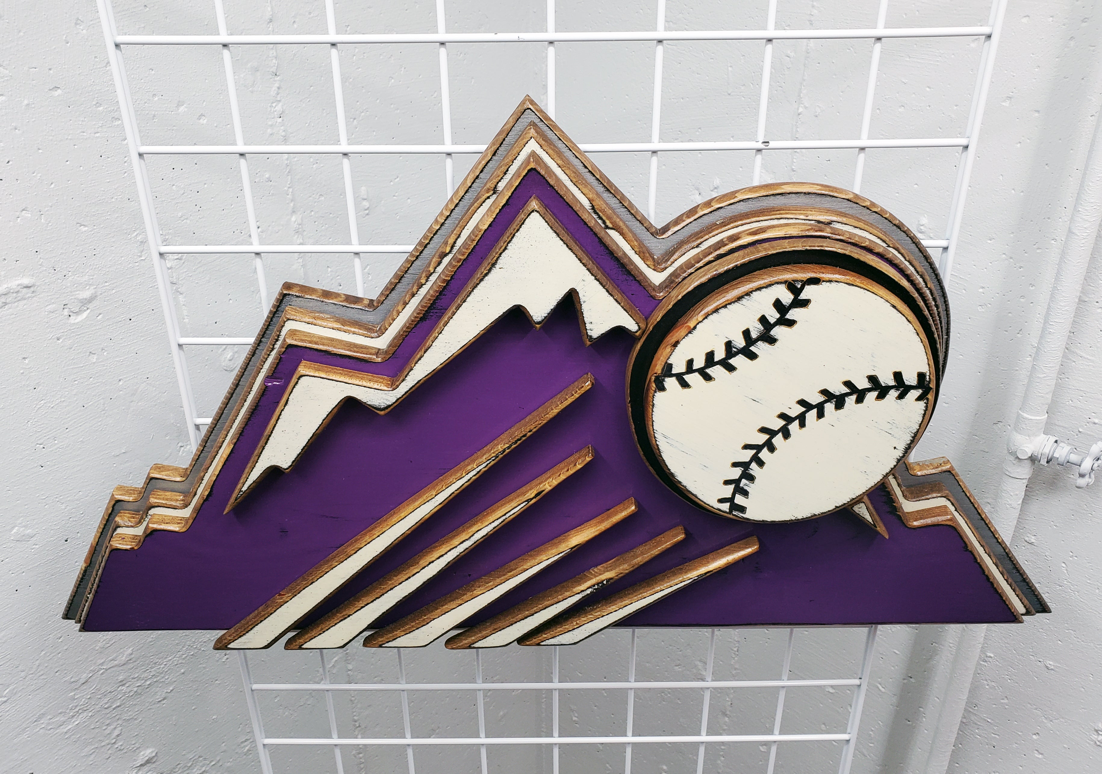 Decorative sign with Colorado Rockies purple mountain design and baseball on a metal grid background